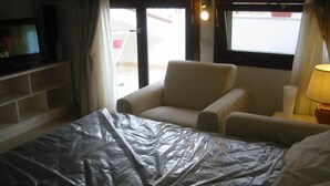 A hotel room with a bed covered in plastic, a chair, a TV, and a window with curtains. - Top floor penthouse apartment with terrace in the historical center, 3 km from the beach (Oristano)