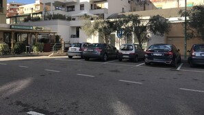 A parking lot with several cars, a building with a sign for a restaurant and pizzeria, and a clear blue sky. - Top floor penthouse apartment with terrace in the historical center, 3 km from the beach (Oristano)