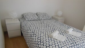 Cama bem arrumada com colcha de padrão geométrico, dois travesseiros brancos e duas mesas de cabeceira brancas com luminárias.
