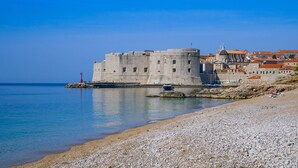 Eine historische Steinburg an einem Kiesstrand mit klarem, blauem Wasser.