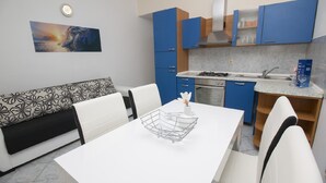A modern kitchen with blue cabinets, a white countertop, and a dining area with a white table and chairs.