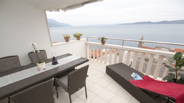 A balcony with a table and chairs, potted plants, and a view of the sea.