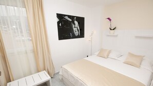 A bedroom with a bed, a bench, a picture on the wall, and a potted plant.