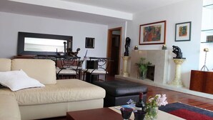 A living room with a beige sofa, a coffee table, and a fireplace with a mantel. There is a dining area with a table and chairs in the background. - Nobel Apartment in Park of Nations.  EXPO, ORIENTE & AQUARIUM VASCO DA GAMA (lisboa)