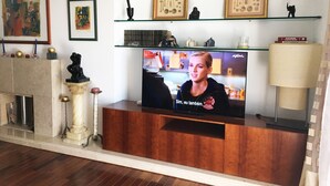 A living room with a wooden entertainment unit, a fireplace, and a television displaying a show. - Nobel Apartment in Park of Nations.  EXPO, ORIENTE & AQUARIUM VASCO DA GAMA (lisboa)