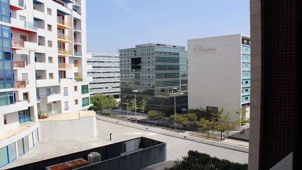 A modern urban landscape with multi-story buildings, including a hotel with balconies and a large glass building. - Nobel Apartment in Park of Nations.  EXPO, ORIENTE & AQUARIUM VASCO DA GAMA (lisboa)