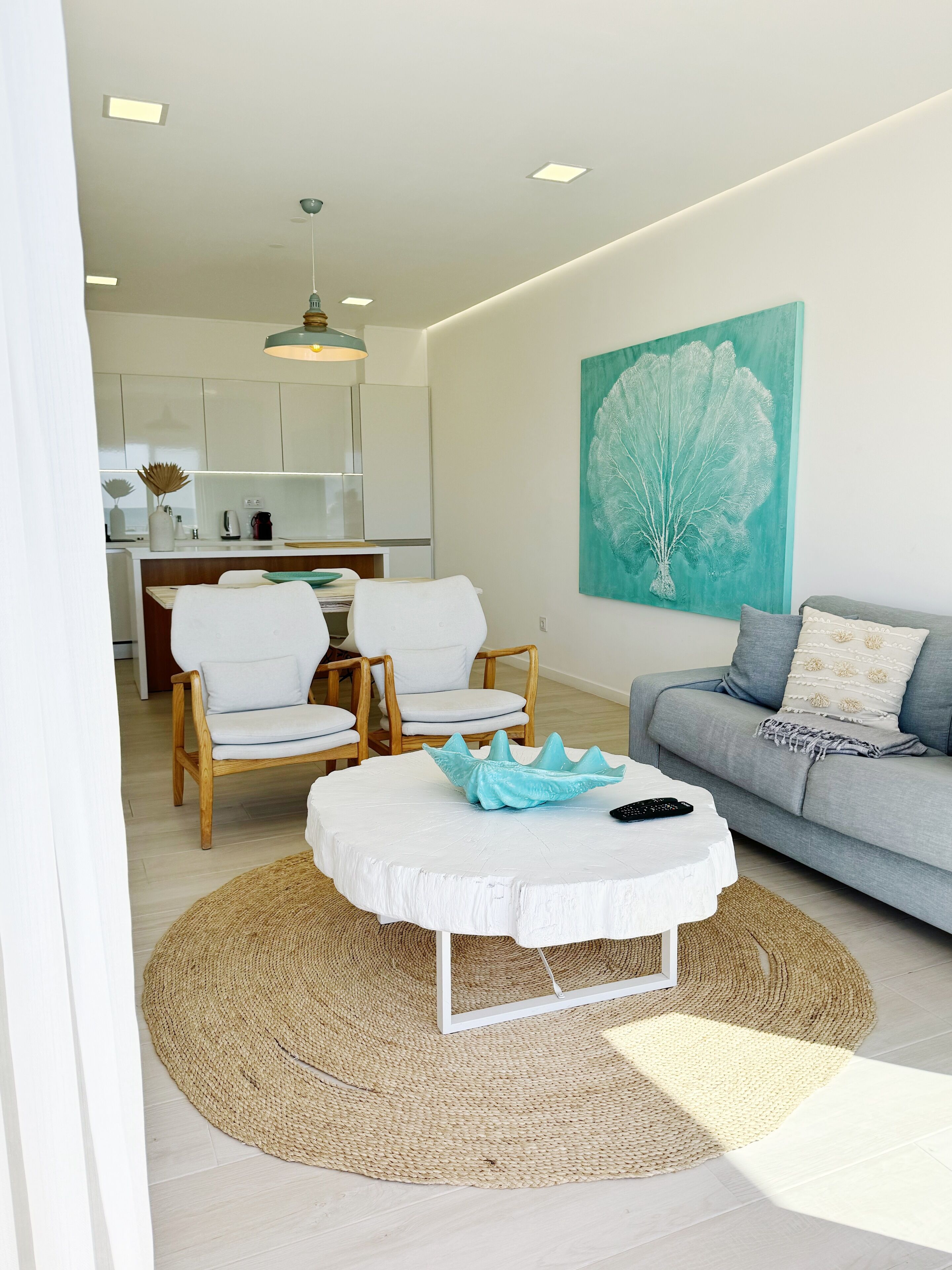A modern living room with a round coffee table, a grey sofa, and a dining area with wooden chairs.
