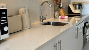 Et moderne køkken med en indbygget ovn, en stålvask og en bordplade med en brødrister og elkedel.