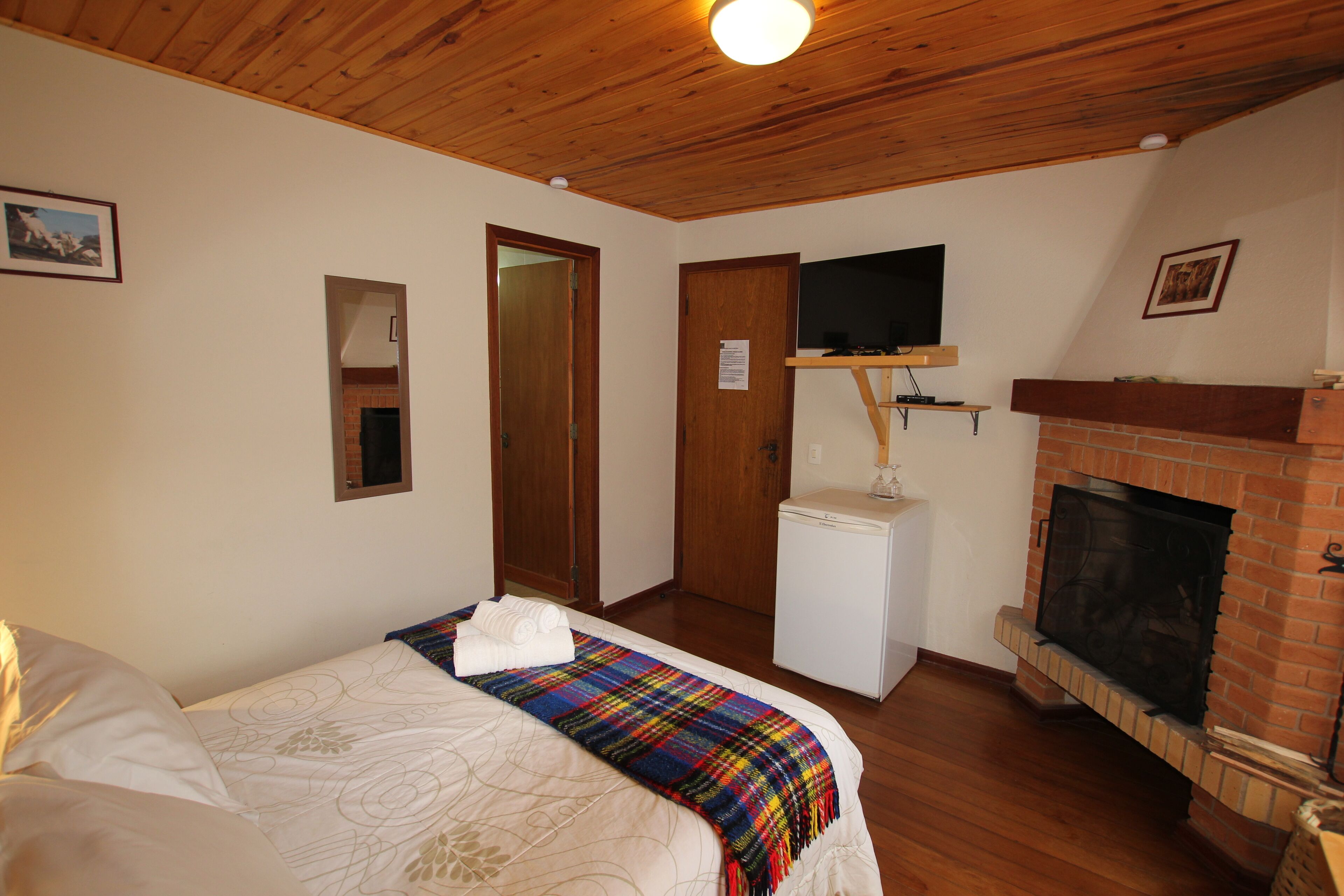 A bedroom with a bed, a television mounted above a fireplace, and a small white appliance.