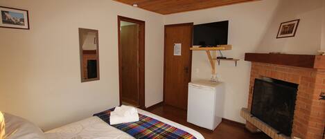 A bedroom with a bed, a television mounted above a fireplace, and a small white appliance.