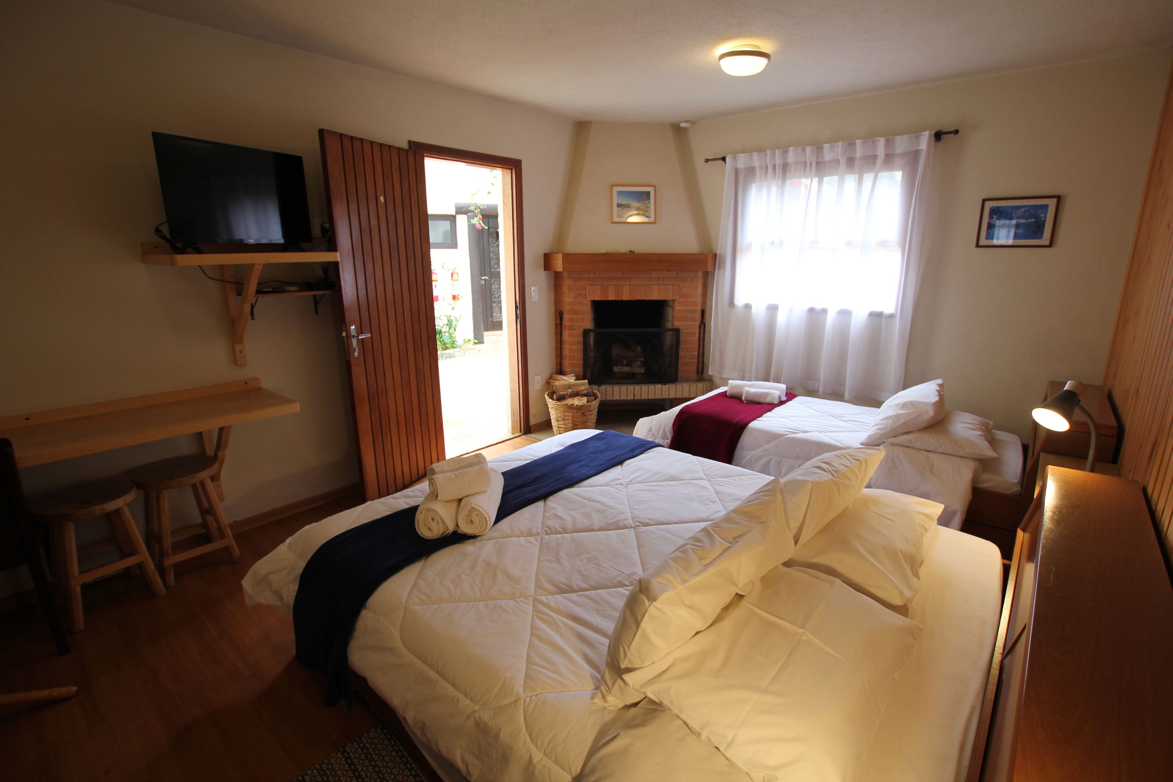Ein Hotelzimmer mit zwei Betten, einem Fernseher auf einem Regal, einem Kamin und einem Schreibtisch mit Stuhl.