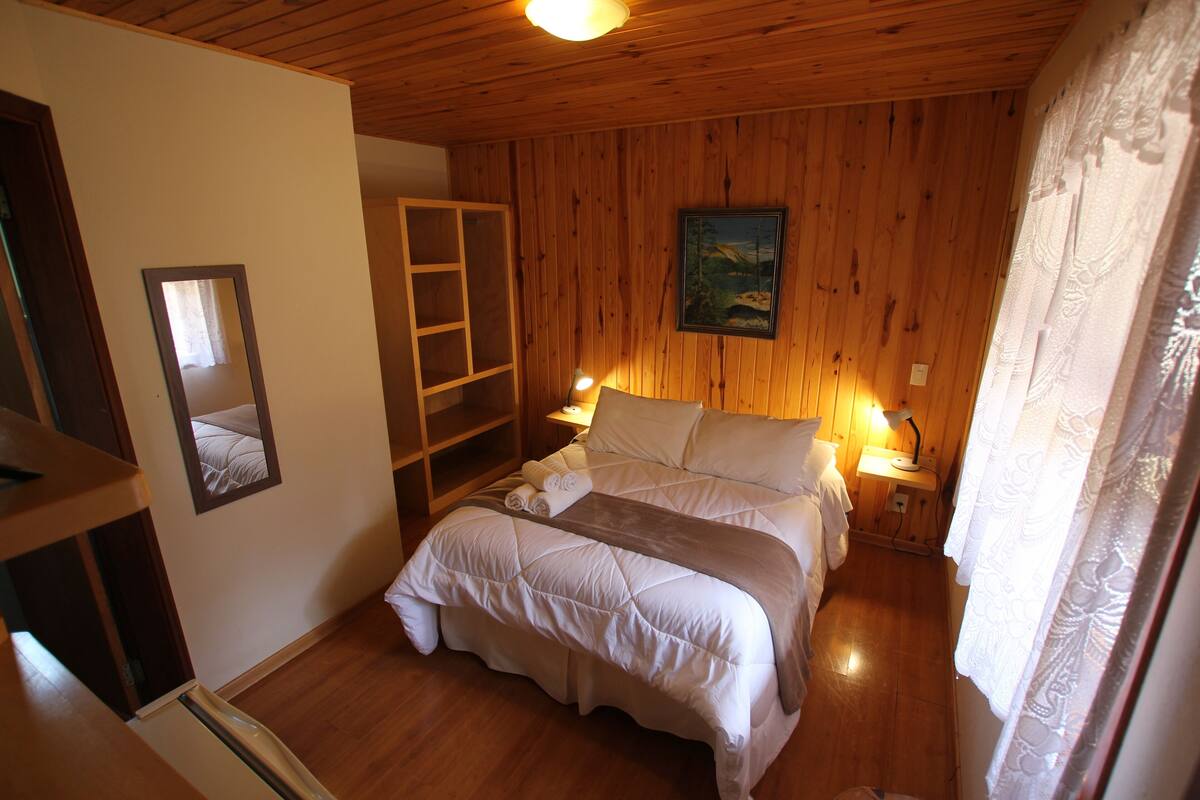Ein Schlafzimmer mit Holzboden, einem Bett mit weißer Bettwäsche, einem Nachttisch mit Lampe und einem Gemälde an der Wand.