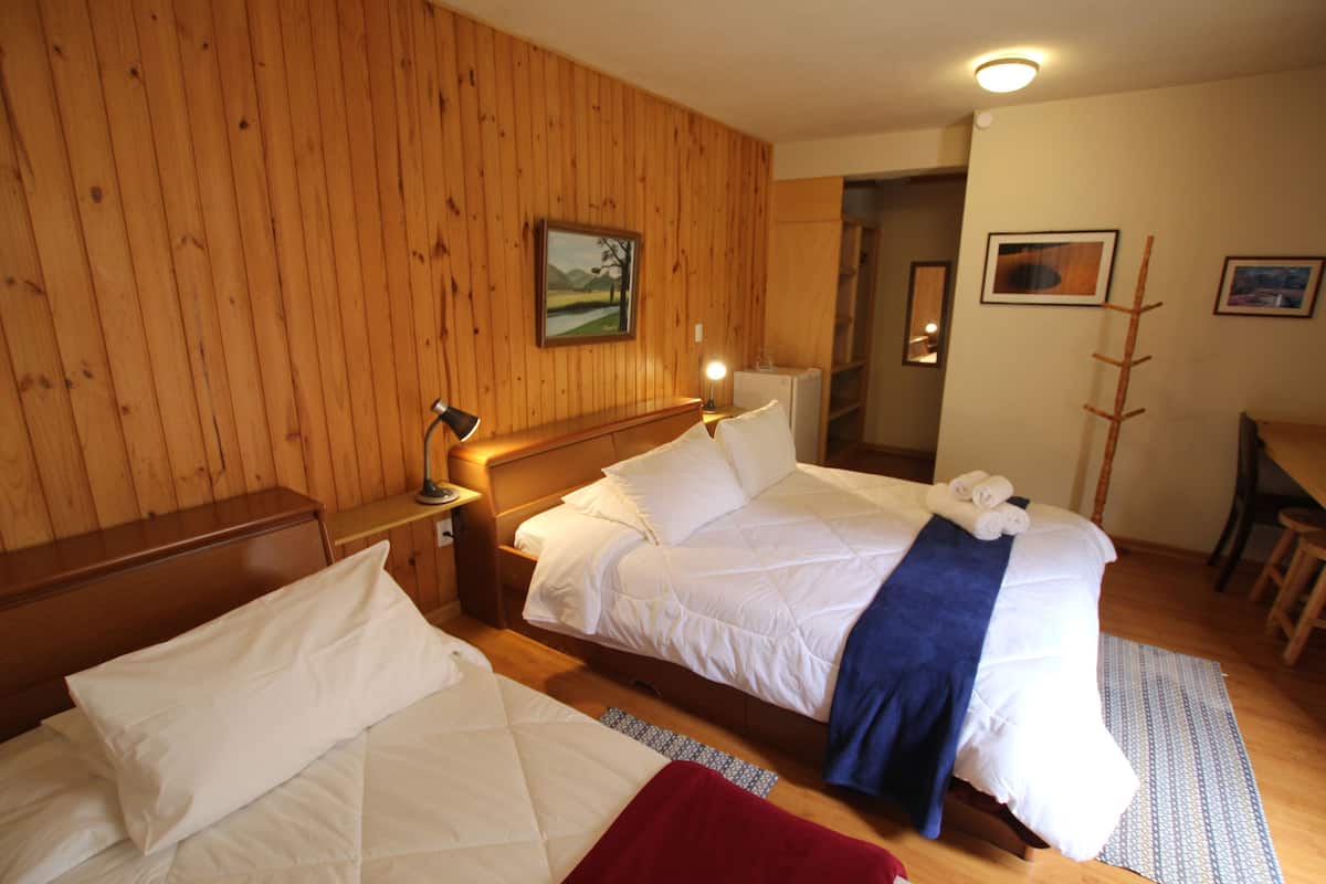 Ein Hotelzimmer mit zwei Betten, Holzwänden, einem Gemälde, einem Schreibtisch und einem Stuhl.