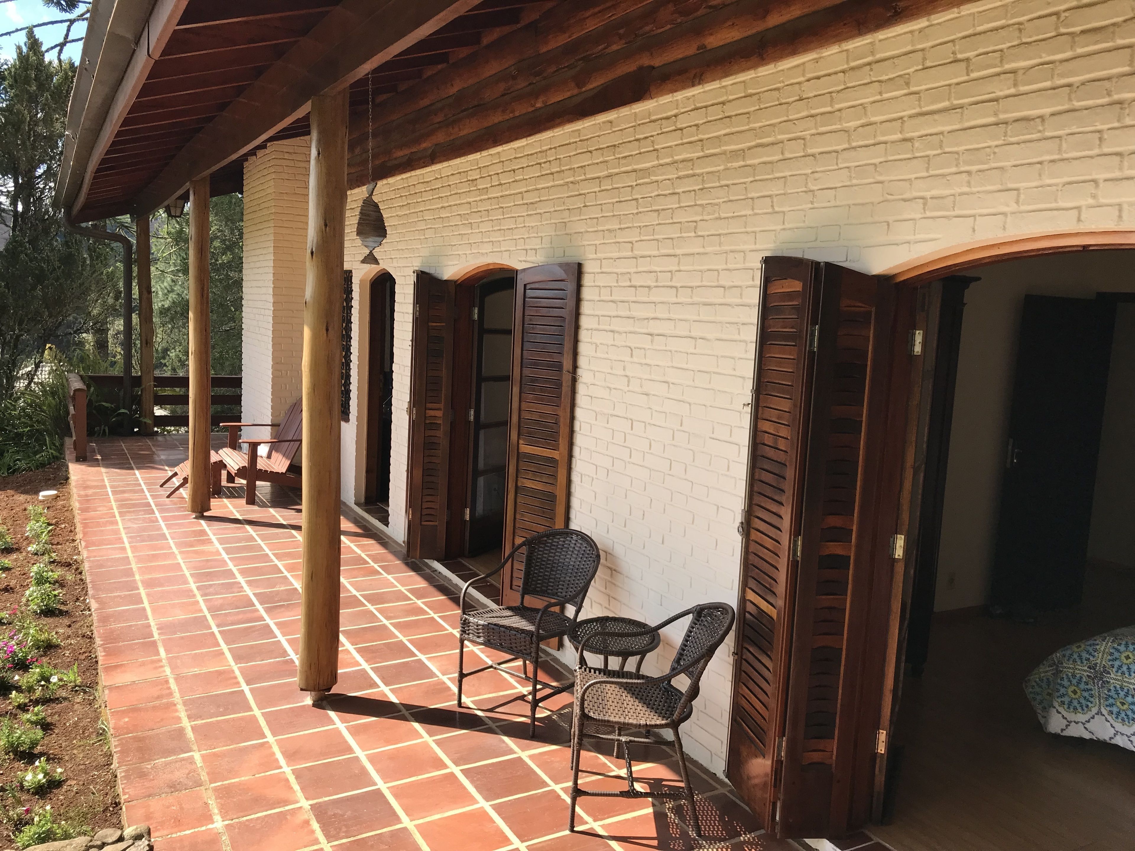 A covered patio with a tiled floor, wooden chairs, and a brick wall.
