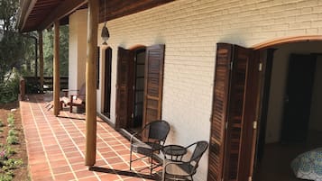A covered patio with a tiled floor, wooden chairs, and a brick wall.