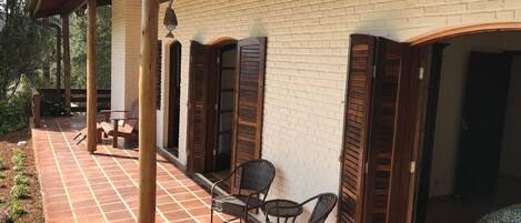 A covered patio with a tiled floor, wooden chairs, and a brick wall.
