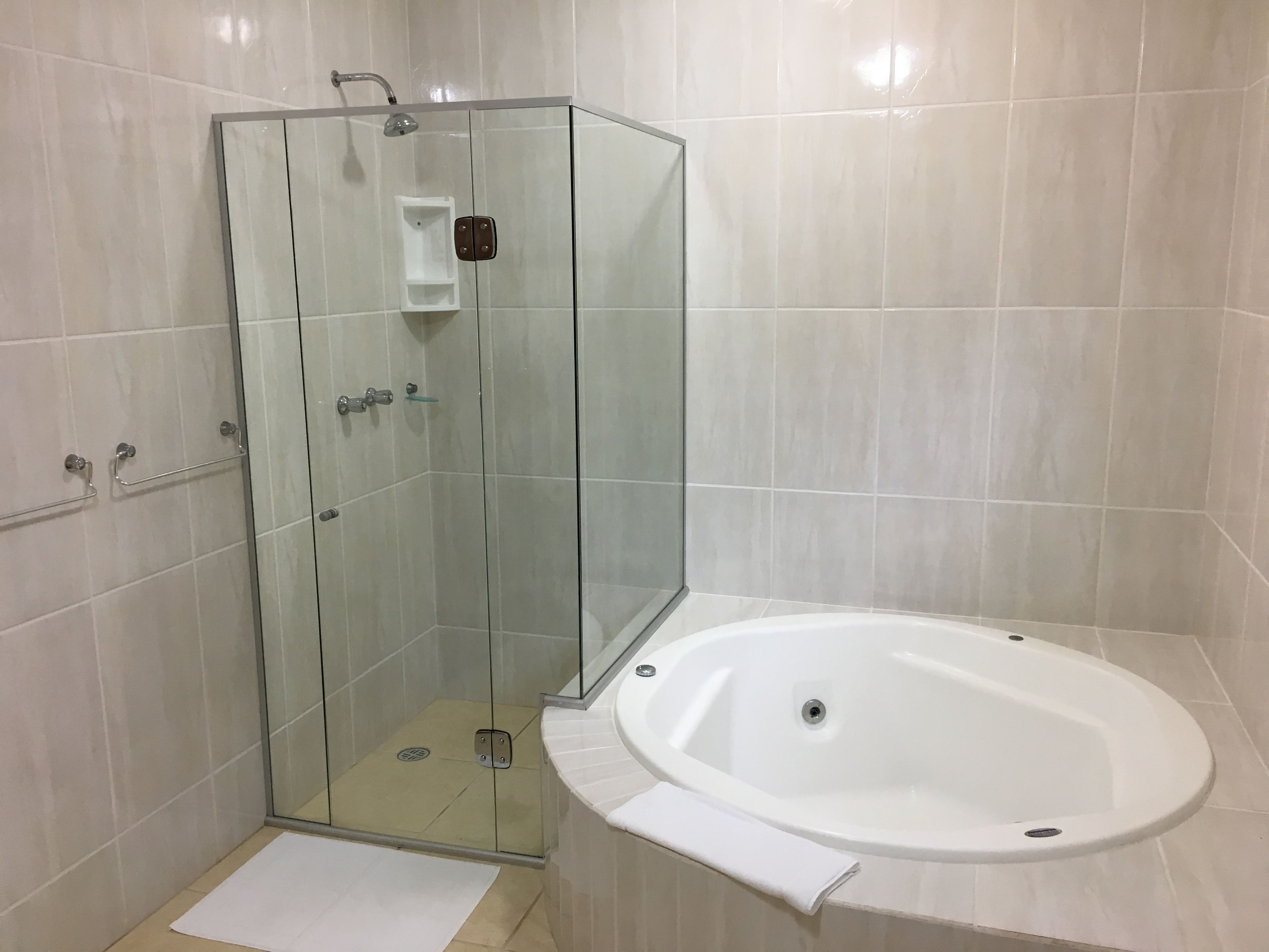 Un baño moderno con ducha envuelta en vidrio, una bañera blanca y un estante pequeño.
