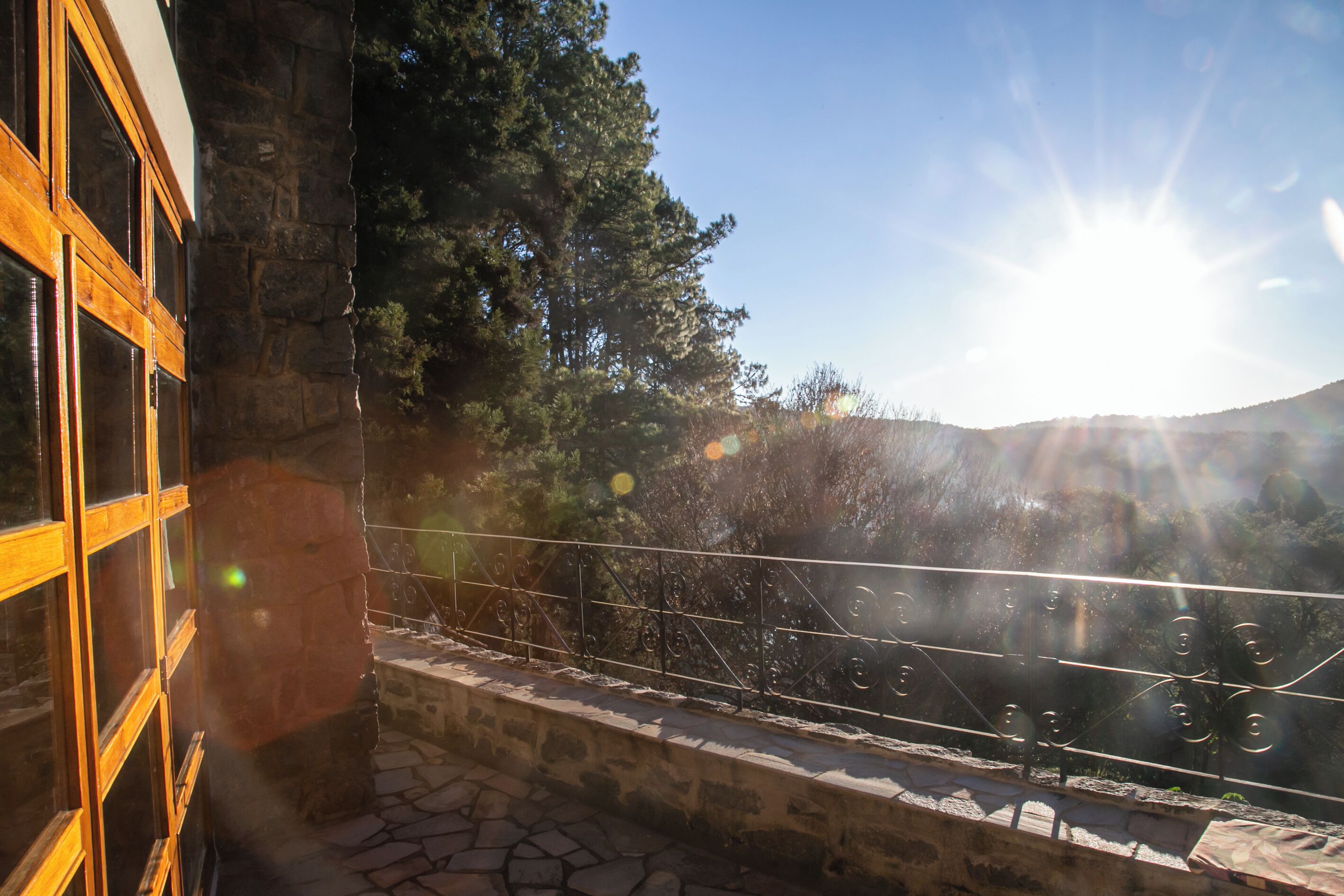Un balcon en pierre avec une balustrade en métal, d’où l’on peut admirer un paysage montagneux.