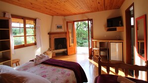 Een kamer met een houten plafond, een open haard, een bed met bloemenbeddengoed, een televisie en uitzicht op groen.