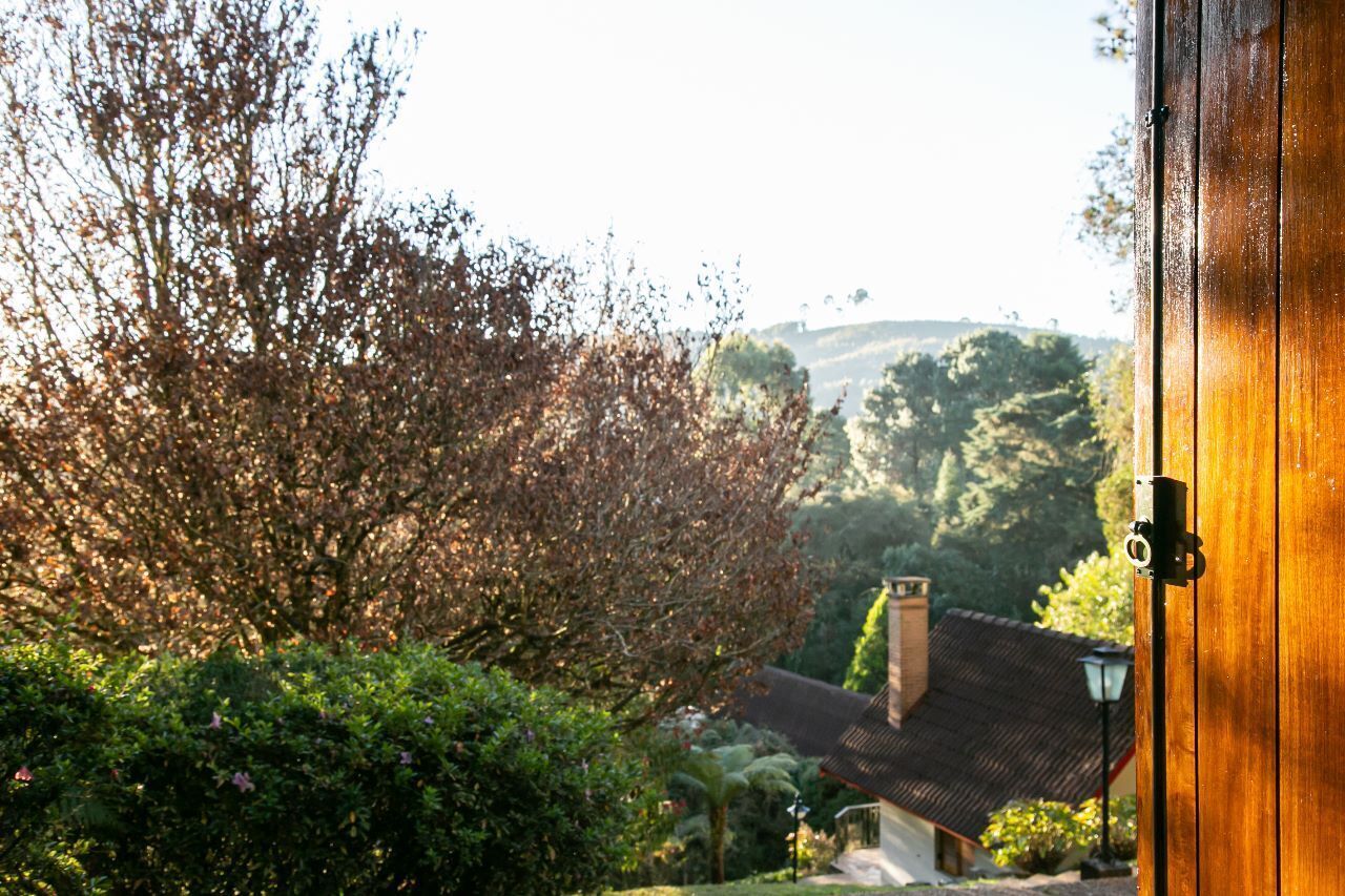 A wooden door with a view of a house and surrounding greenery.