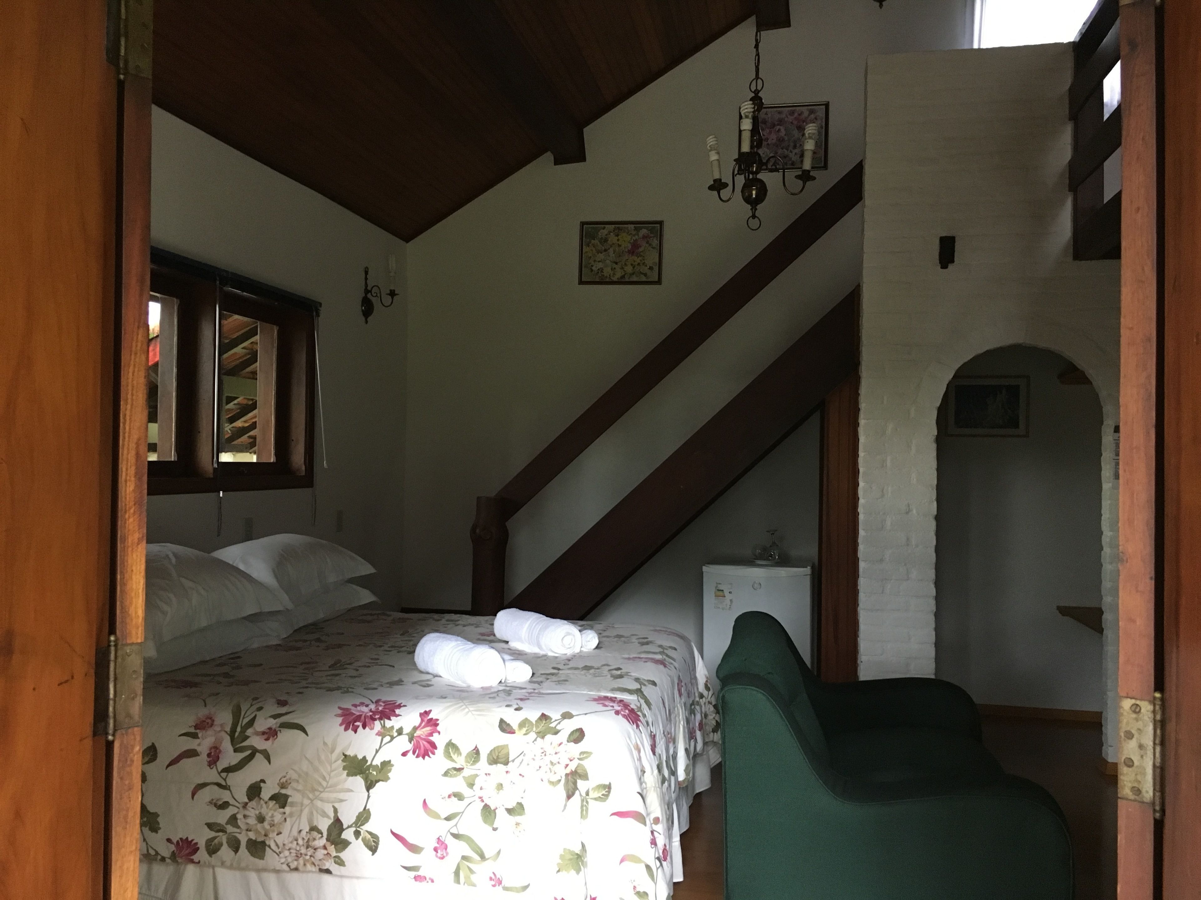 Ein Schlafzimmer mit einem Bett, einem grünen Sessel, einer Kristallleuchtre und einer Treppe.
