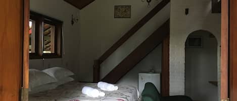 Une chambre à coucher avec un lit, un fauteuil vert, un lustre et un escalier.
