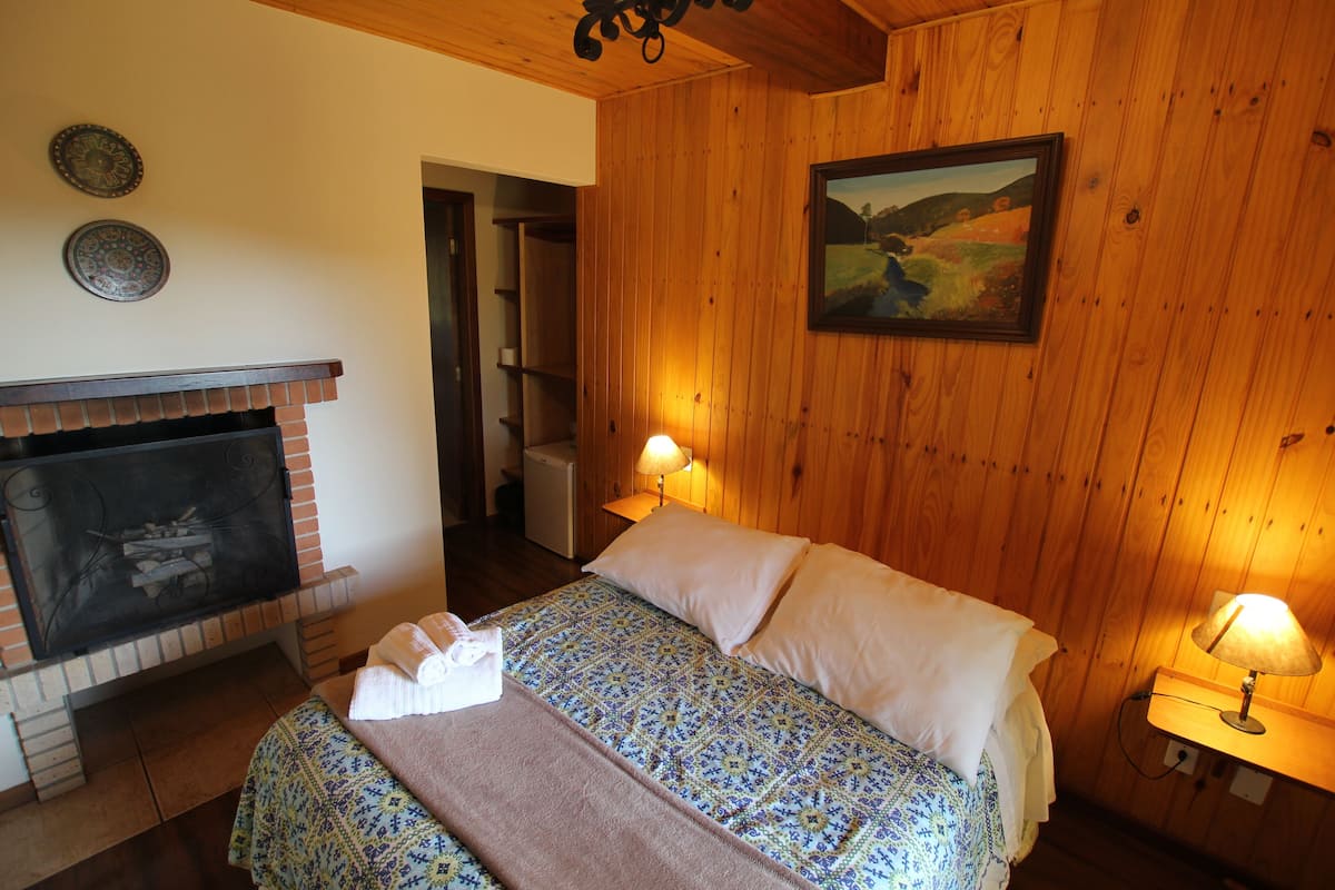 Ein gemütliches Zimmer mit Kamin aus Ziegelsteinen, einem Bett mit gemusterten Textilien und einem Bild an der Wand.