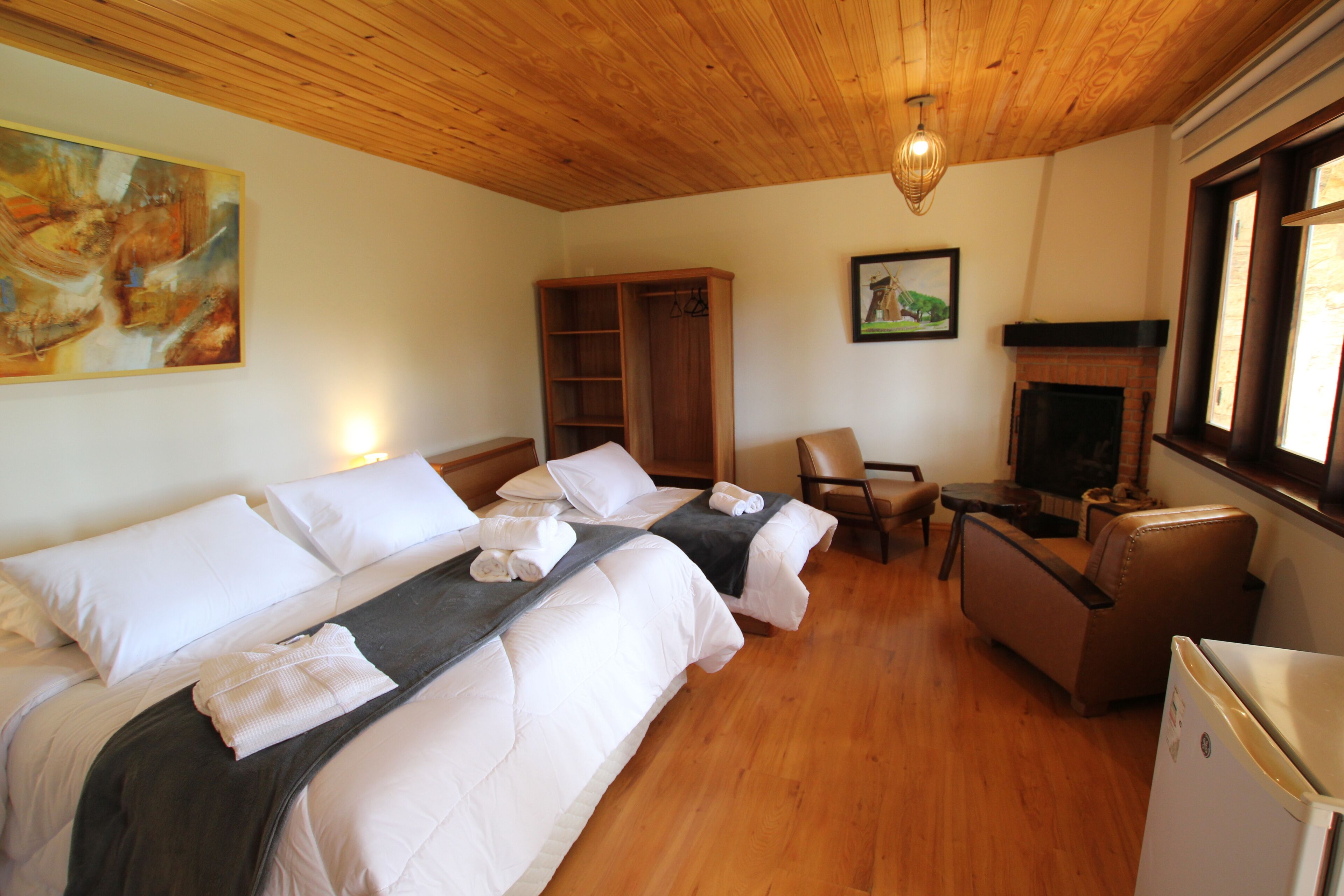 A hotel room with two beds, a wooden ceiling, a fireplace, a TV, and a painting on the wall.