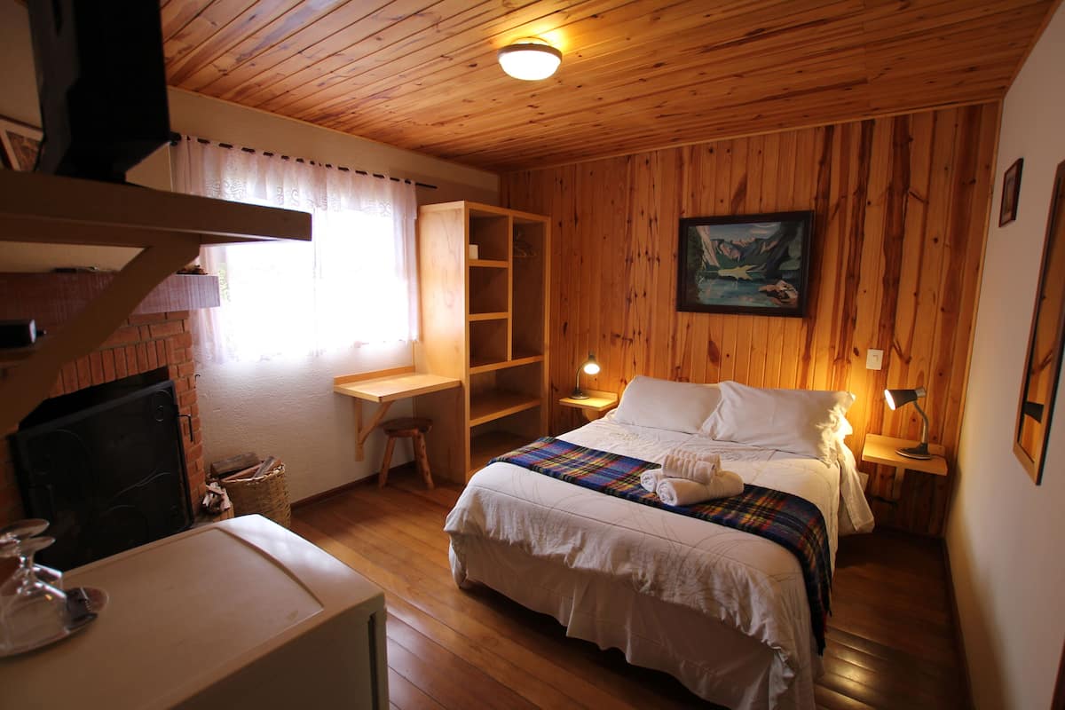 Ein Zimmer mit Holzwänden, einem Bett, einem Schreibtisch, einem Sessel, einem Kamin und einem Gemälde an der Wand.