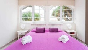 A bedroom with a large bed, two nightstands, and a window with a view of palm trees. - Cozy home in Tenerife with views & pool (Santa Cruz de Tenerife)