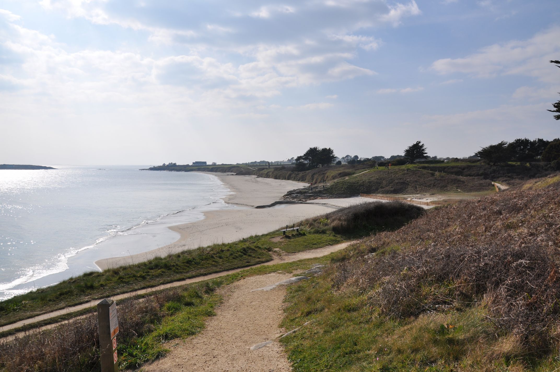 A coastal path leading to a beach with a clear view of the ocean and distant land.
