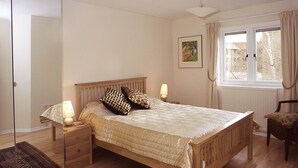 Un dormitorio con una cama de madera, lámparas de noche, una ventana con cortinas, una silla y un espejo.