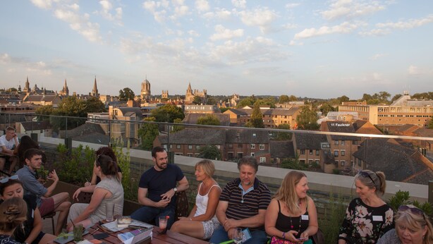 Un grupo de personas sentadas en una terraza con vistas a un paisaje urbano.