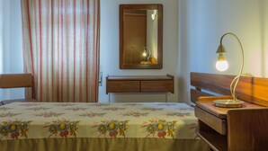 Quarto de hotel com cama, mesa de cabeceira de madeira, espelho e abajur.