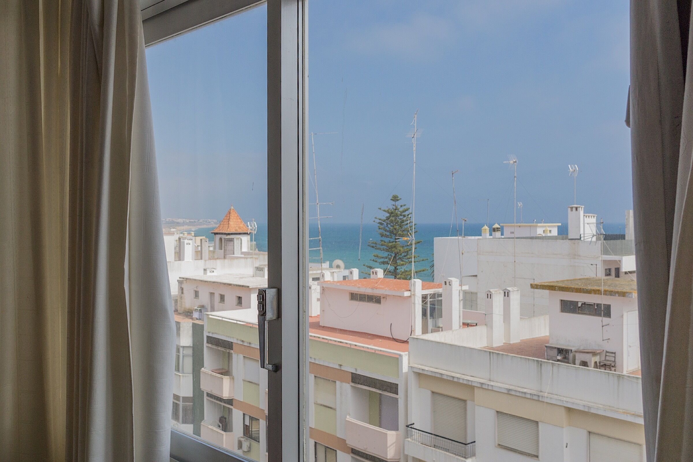 A view from a window overlooking a coastal cityscape with buildings and a clear sky.