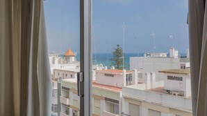 Vista da janela sobre uma paisagem urbana costeira, com edifícios e céu claro.