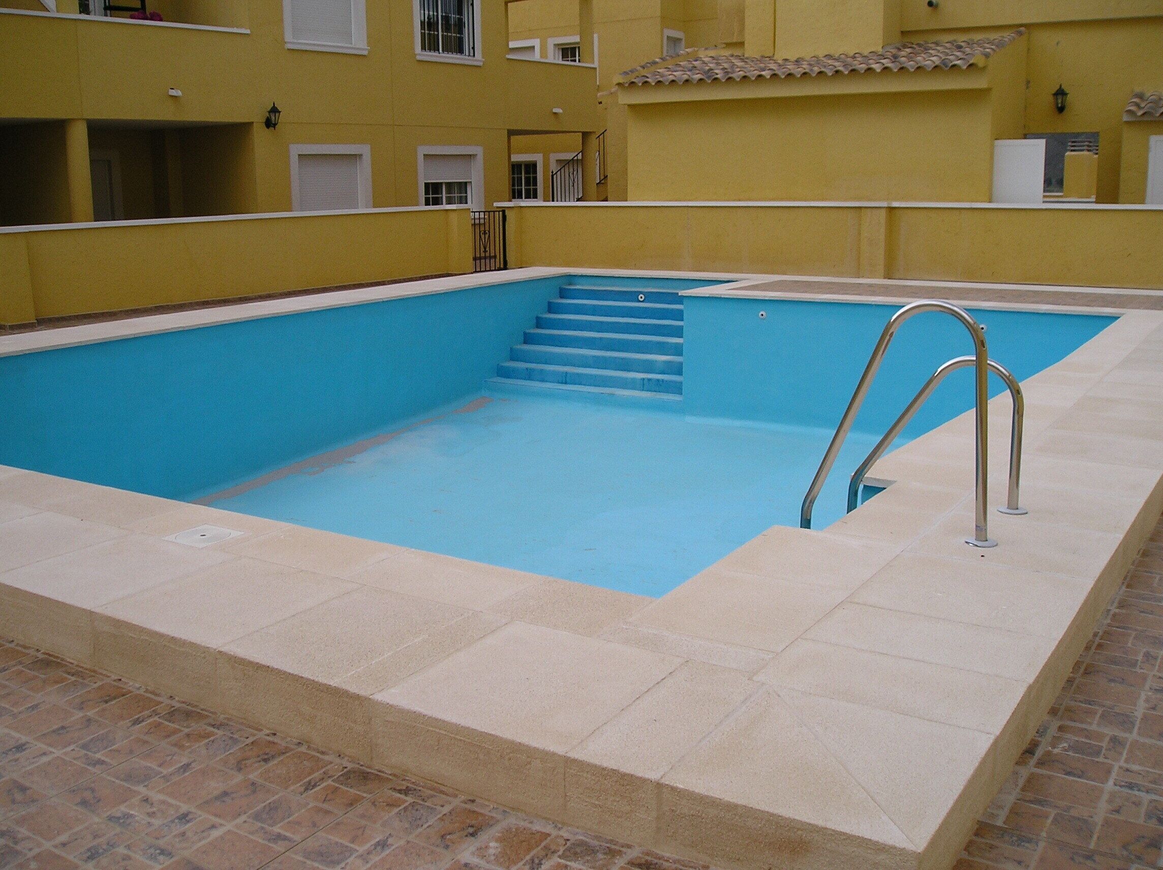 A rectangular swimming pool with a blue interior, surrounded by beige tiles and a brick border.