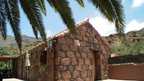 A stone building with a tiled roof, surrounded by palm trees and a desert landscape. - Rural House La Fuente de la Flora (Valle, El (Santa Lucia De Tirajana))