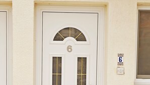 A white door with the number 6, a welcome mat, and a small window with a number 6 sign on the wall.