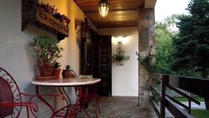 Une terrasse extérieure couverte, dotée d’un sol en pierre, de chaises en métal rouge, d’une petite table ronde et de plantes en pot.