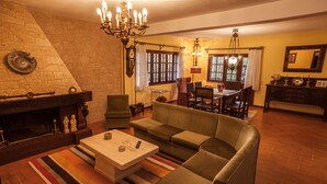 Un salon chaleureux avec une cheminée, un canapé, une table basse et un coin repas agrémenté d’un lustre.