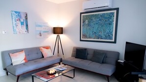 A modern living room with two grey sofas, a coffee table, a floor lamp, a TV, and artwork on the walls.