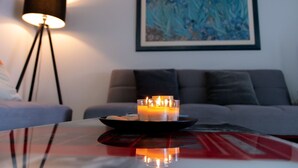 A room with a table holding candles, a floor lamp, and a painting on the wall.