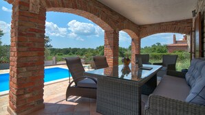 Eine Terrasse im Freien mit einem Tisch mit Glasplatte, Korbmöbeln und Blick auf einen Swimmingpool.