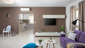 A modern living room with a sofa, a coffee table, and a TV. There is a kitchen in the background with cabinets and a sink. - Villa Meli in Vodnjan (Vodnjan)
