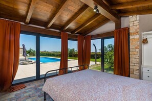A bedroom with a view of a swimming pool, wooden ceiling beams, and a brick wall. - Villa Meli in Vodnjan (Vodnjan)