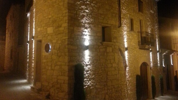 A stone building with multiple windows and a central door, illuminated by artificial lighting at night.