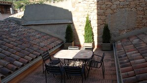 A rooftop patio with a table and chairs, surrounded by stone walls and potted plants.