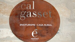 A circular sign with the text "cal gasset" and "ENOTURISME - CASA RURAL" on a stone wall.