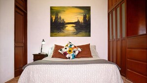 Una camera da letto con un letto, un comodino, una lampada, un quadro che raffigura una veduta cittadina e porte in legno.